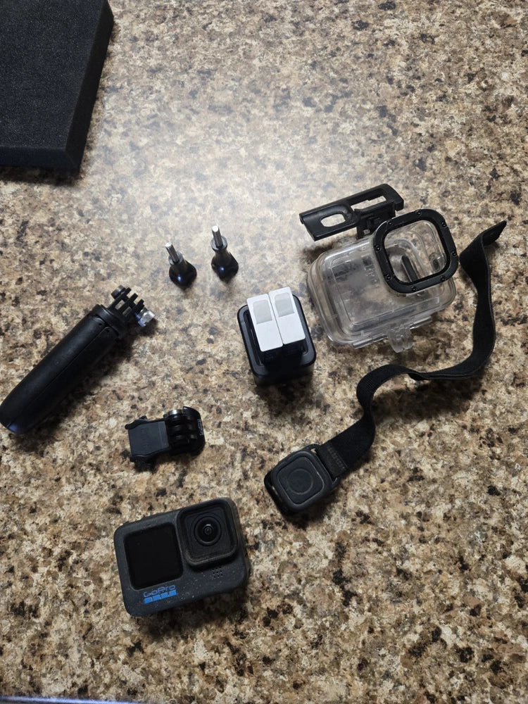 Black action camera with clear waterproof case and mounting accessories, plus battery door