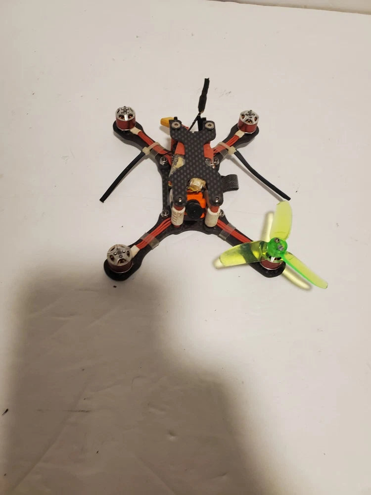 FPV quadcopter drone with orange-and-black frame, four arms, propellers and antenna