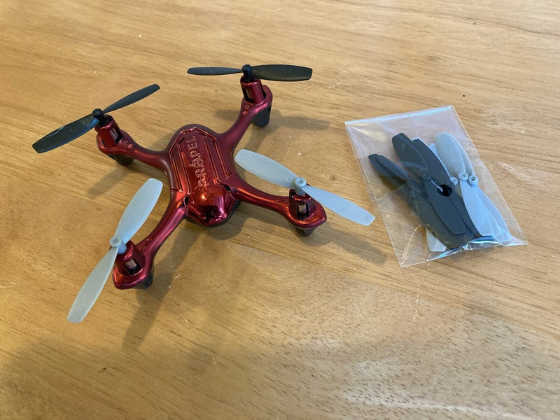 Red mini drone with four propellers and extra blades in a clear plastic bag