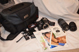 Canon DSLR camera kit with black bag, two lenses, camera body, and instruction cards