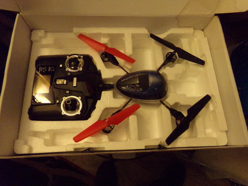 Black quadcopter drone kit in open box with controller and red propellers