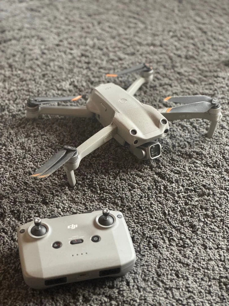 Gray quadcopter drone with handheld controller, both resting on carpet
