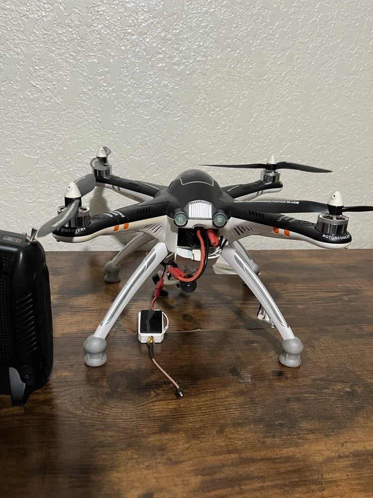 Quadcopter drone with black arms, silver landing legs and four propellers, exposed wiring.