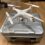 White quadcopter drone with camera and four propellers, shown on a carrying case base
