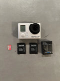 Silver action camera with black lens, plus two SanDisk microSD cards and GoPro mount card
