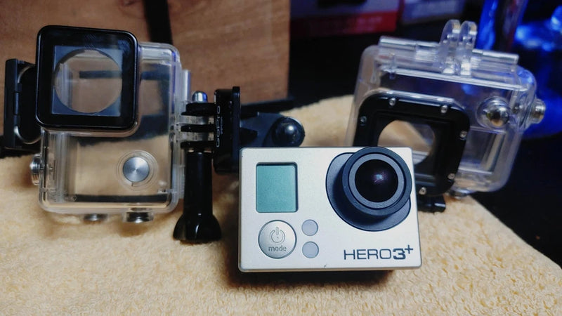 Silver action camera with black lens, front view, in clear waterproof housing