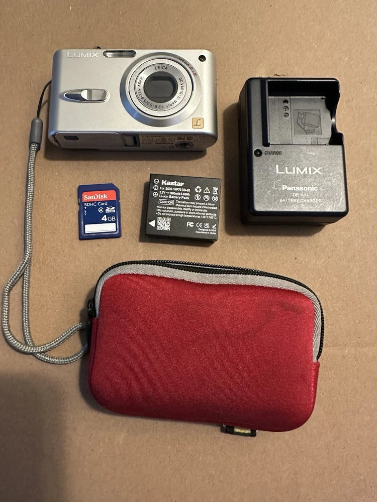Silver digital camera with charger, battery, SD card, and red zip case