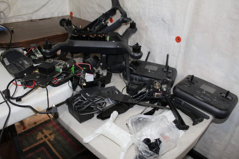 Drone lot with two black quadcopters, controllers, cables, and loose parts