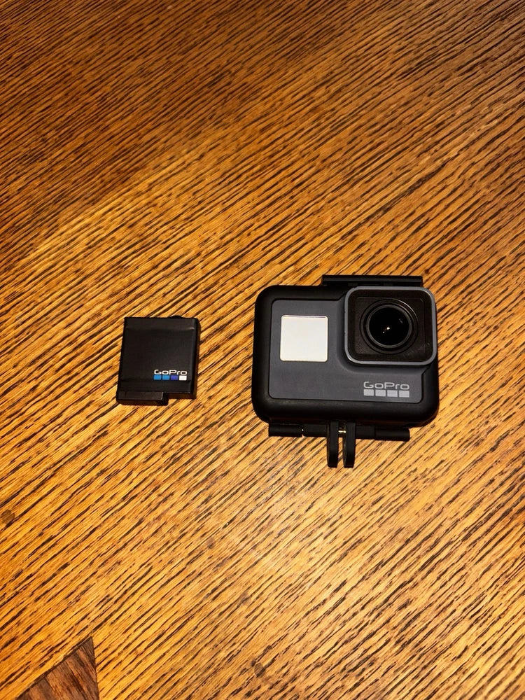 Black action camera with front LCD screen and lens, shown with small accessory