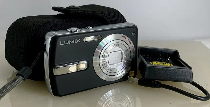 Compact digital camera with LUMIX logo, black and silver body, visible lens dial and strap