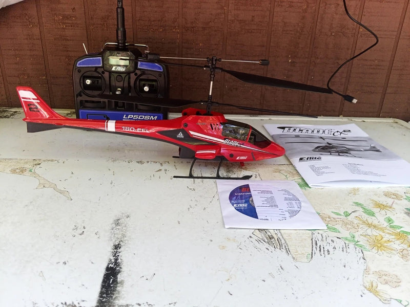 Red RC helicopter model with rotor mast and skids, hobby controller nearby