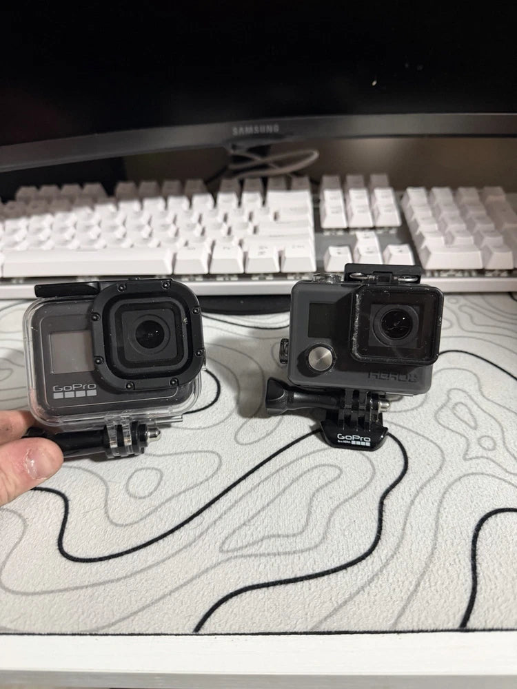 Two black action cameras in waterproof housings with mounts and doors, side-by-side
