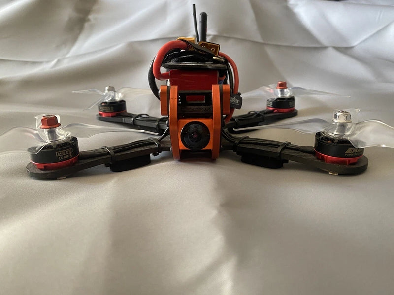 Racing drone with four arms, orange camera mount, red motor caps