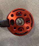 Red mini drone motor with circular housing, mounting holes, and exposed copper windings