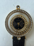 Ladies Gruen quartz wristwatch with black dial, gold-tone case, rhinestone bezel, black leather strap