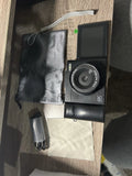 Digital camera with open LCD screen and large lens, with pouch, cable, and cloth