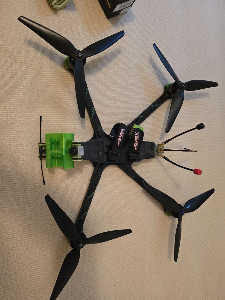 Black FPV quadcopter drone with four propellers and green battery mount