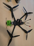 Black FPV quadcopter drone with four propellers and green battery mount