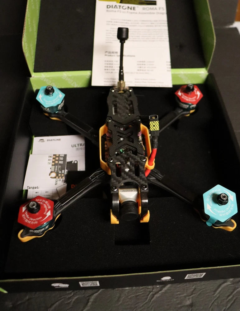 Quadcopter drone with orange frame, four arms and visible propellers in a box