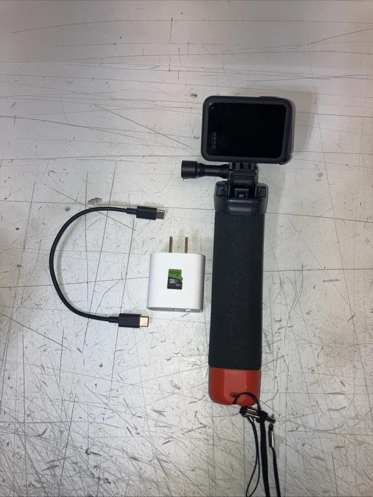 Black action camera mounted on a handle with cables and a small adapter