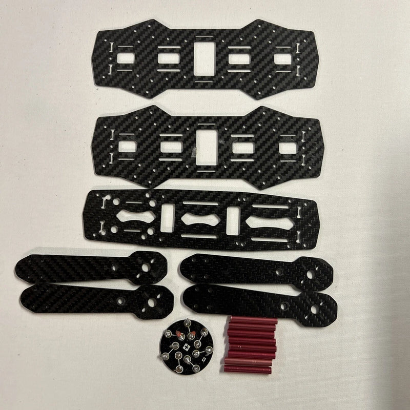 Quadcopter drone assembly kit parts: carbon-fiber arms, mounting plates, circuit board, red wires