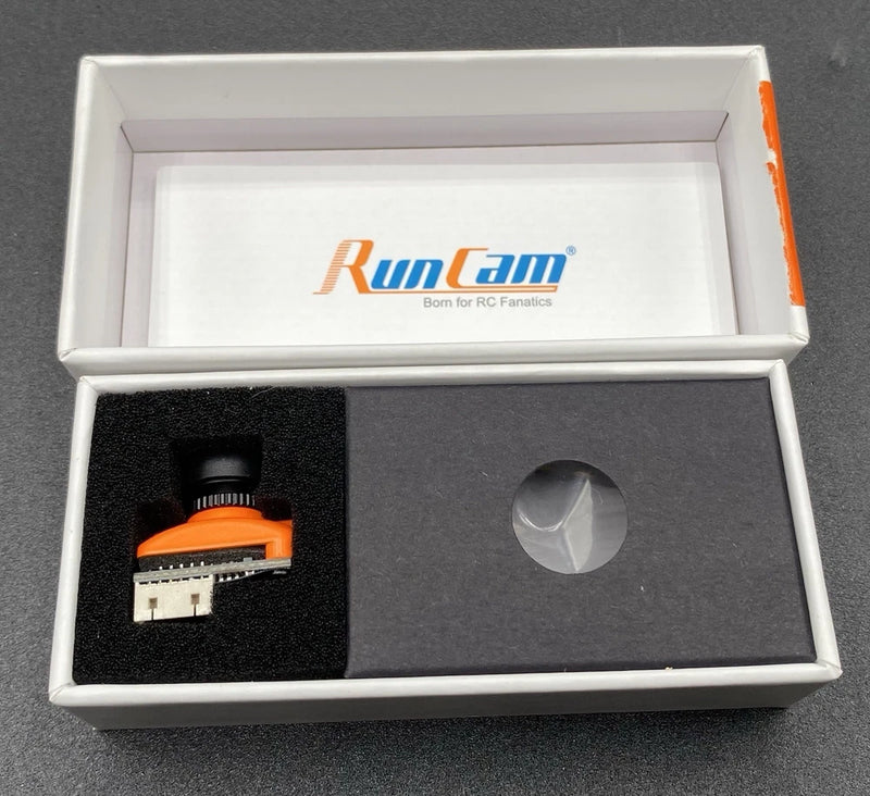 Micro Swift3 FPV camera module in open box, showing orange connector and lens cap
