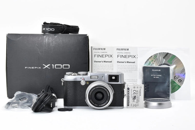 Silver compact digital camera with lens, manuals, and included accessories