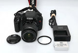 Canon DSLR camera with 18–55mm lens, lens cap, strap, battery charger, and filter