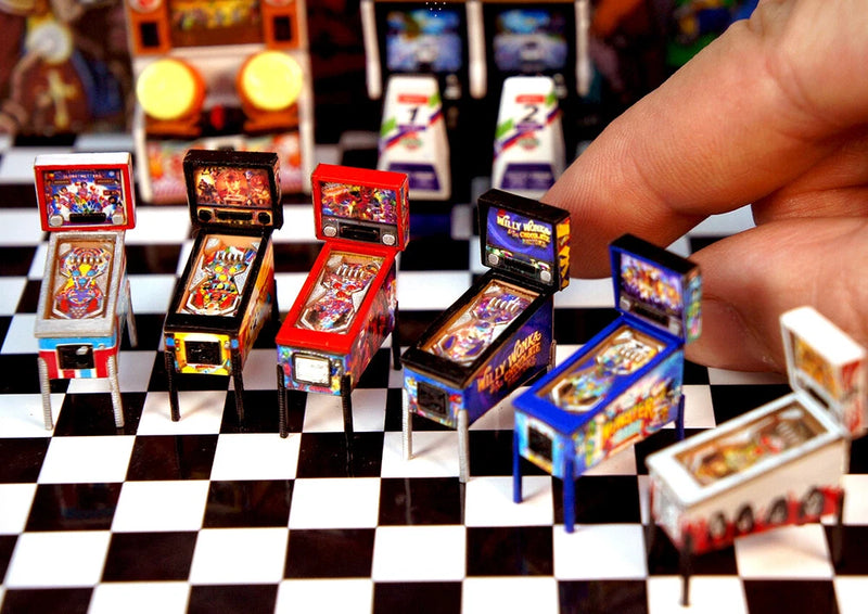 Mini arcade game cabinet model set with colorful screens, handheld by a finger