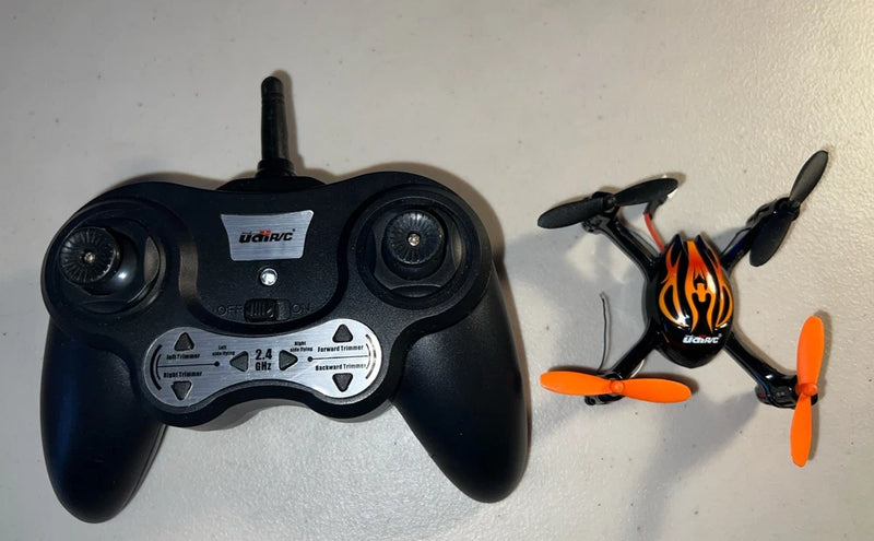 Black remote controller and small quadcopter drone with orange prop blades and flame decal