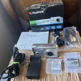 Silver compact digital camera with accessories kit, cables, battery charger, manual, and box