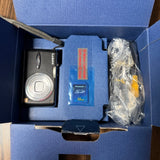 Black digital camera in retail box with lens and wrapped accessories