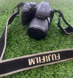 Black Fujifilm digital camera with attached lens and shoulder strap, front view
