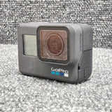 GoPro HERO6 action camera, gray body with front lens window and side buttons.
