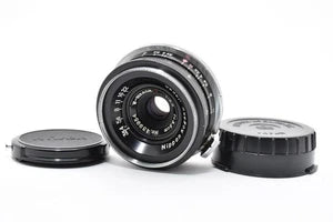 Black Nippon Kogaku Nikkor camera lens with front element and two caps